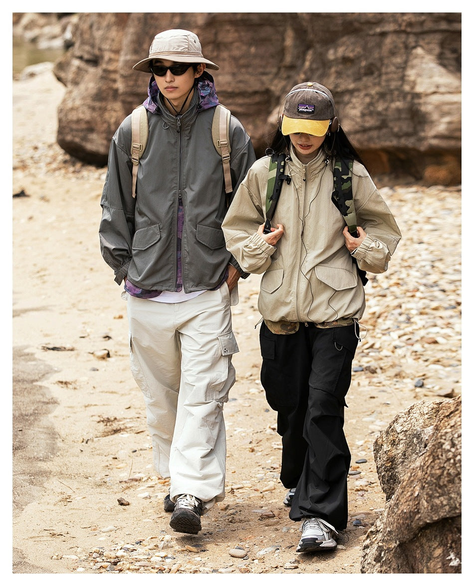 Two hikers walk outdoors in oversized jackets: cream on the woman and gray on the man, shown with cargo pants.