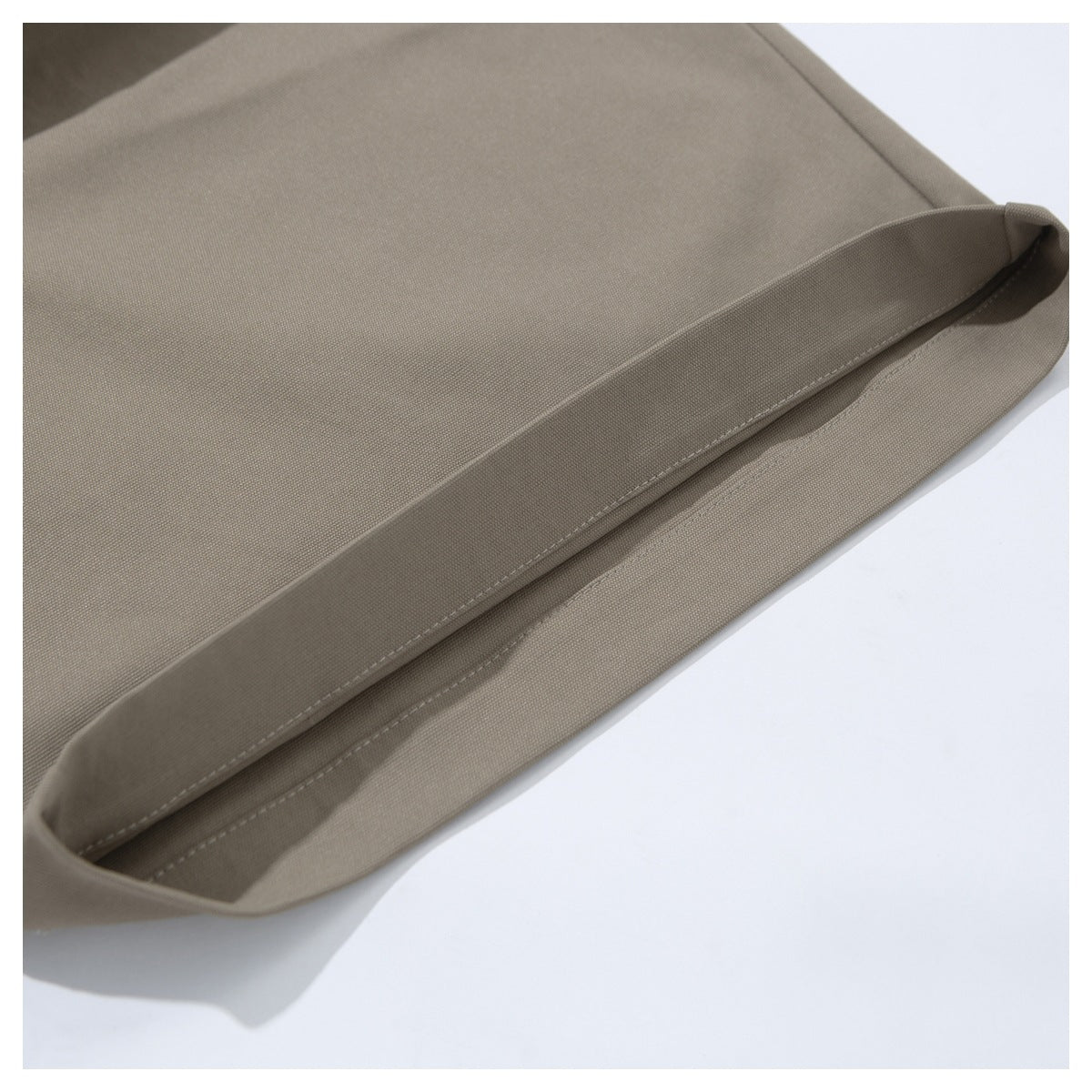 Close-up of the stitched hem on taupe trousers.