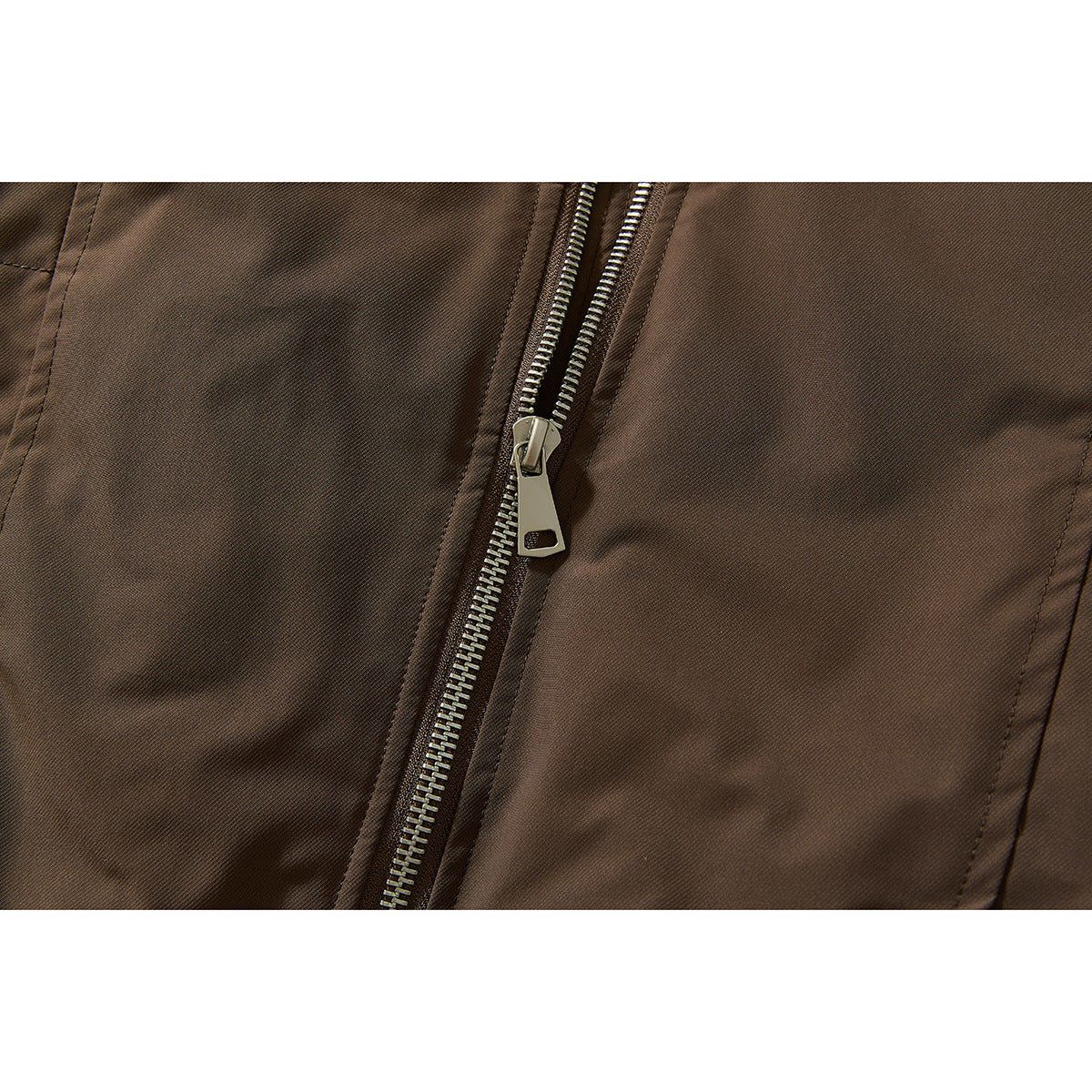 Close-up of the brown jacket's metal zipper, pull, and stitched panels.