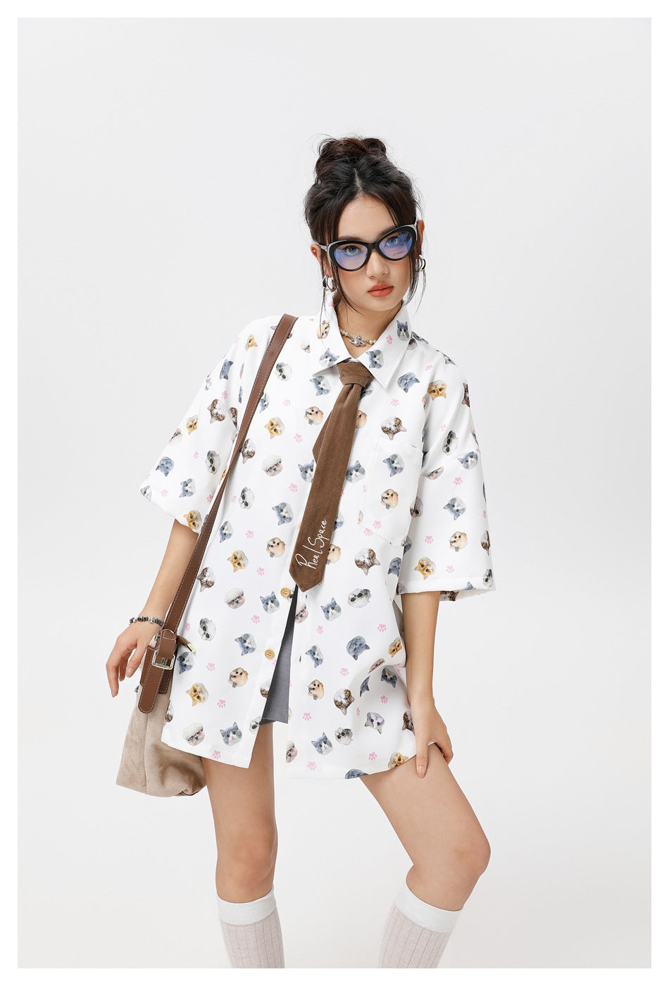 Model wearing a white oversized cat-print shirt with pink paw prints, brown tie, and gray shorts, shown from the front.