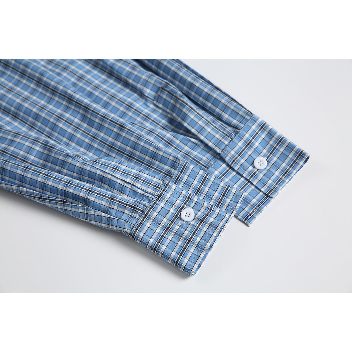 Close-up of blue plaid shirt cuffs with white buttons, laid over the sleeves of a heather gray polo.