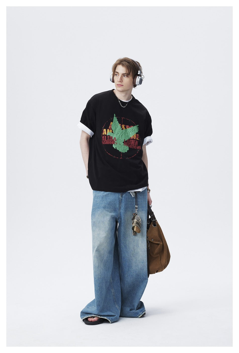 Model in a black T-shirt with a raised green bird graphic, white rolled sleeve layers, and wide-leg blue jeans.