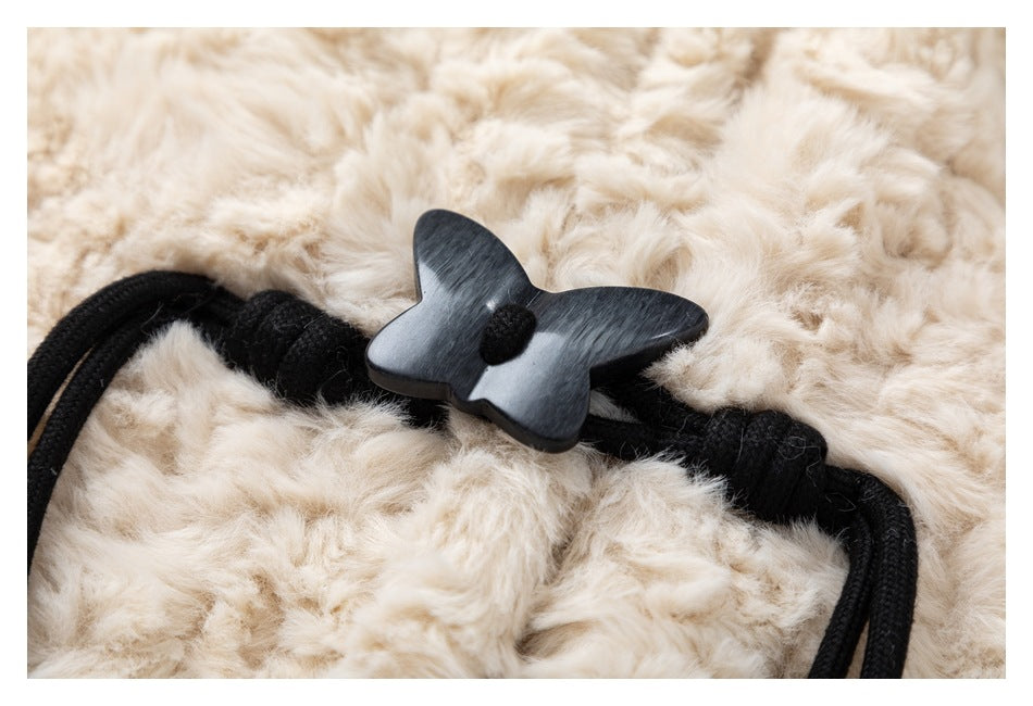 Close-up of a black butterfly-shaped toggle and cord against the ivory plush coat.