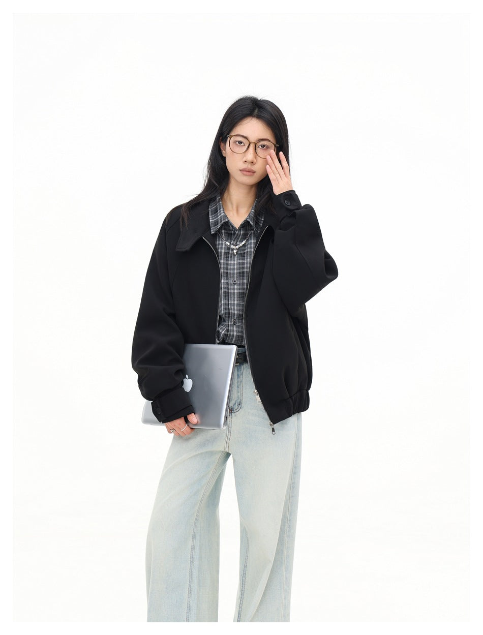Closer view of a model wearing an open black jacket over a gray plaid shirt and pale jeans.