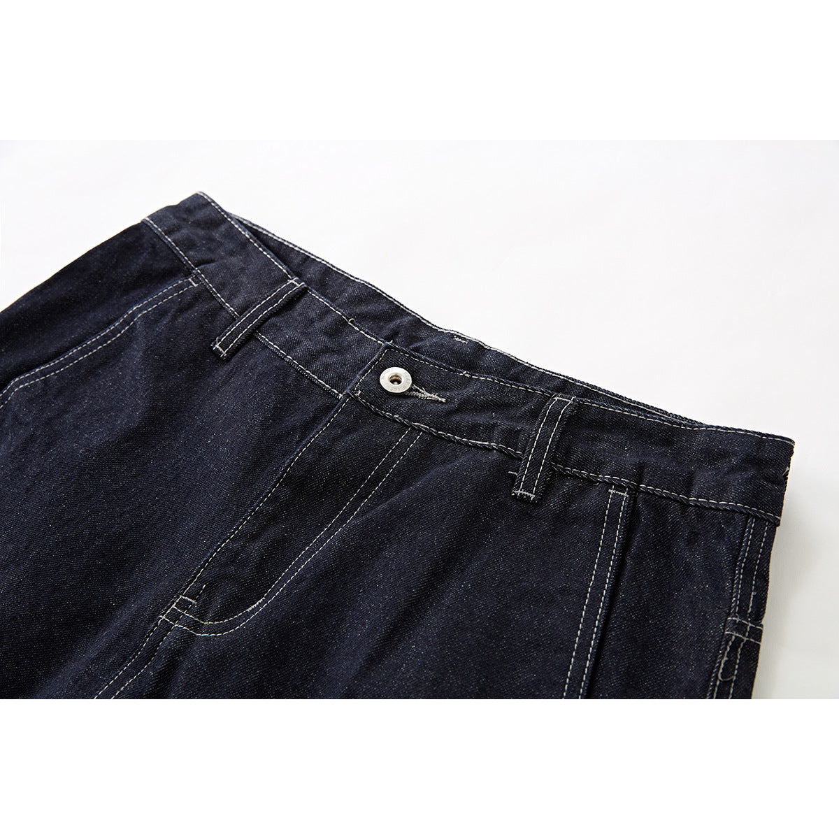 Close-up of dark indigo denim shorts showing the waistband, button, belt loops, fly, and pale contrast stitching.