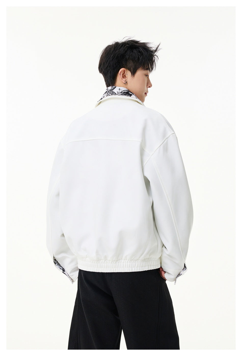 Rear view of a model wearing a white jacket with a black floral-print collar and elasticized hem.