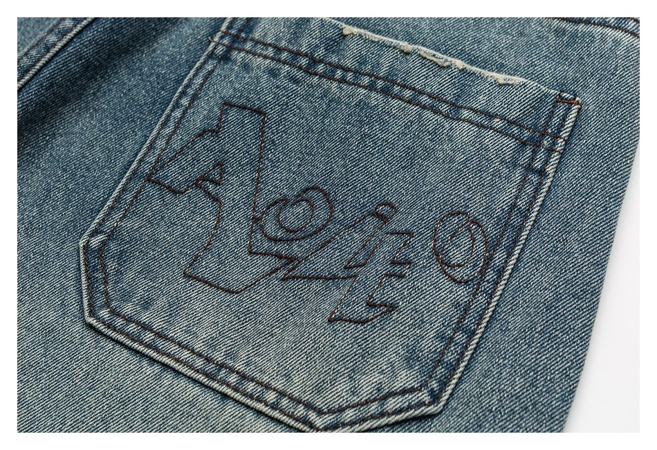 Close-up of a blue denim back pocket with a large abstract dark stitched graphic.