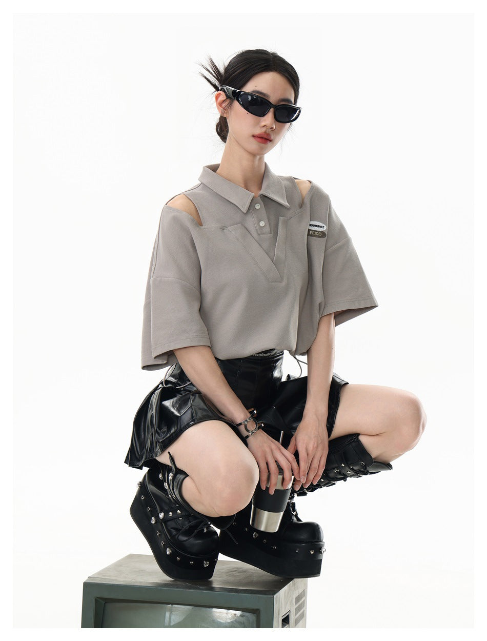 Model crouching in a taupe cutout-shoulder polo top with a V-shaped front panel and drawstring hem.