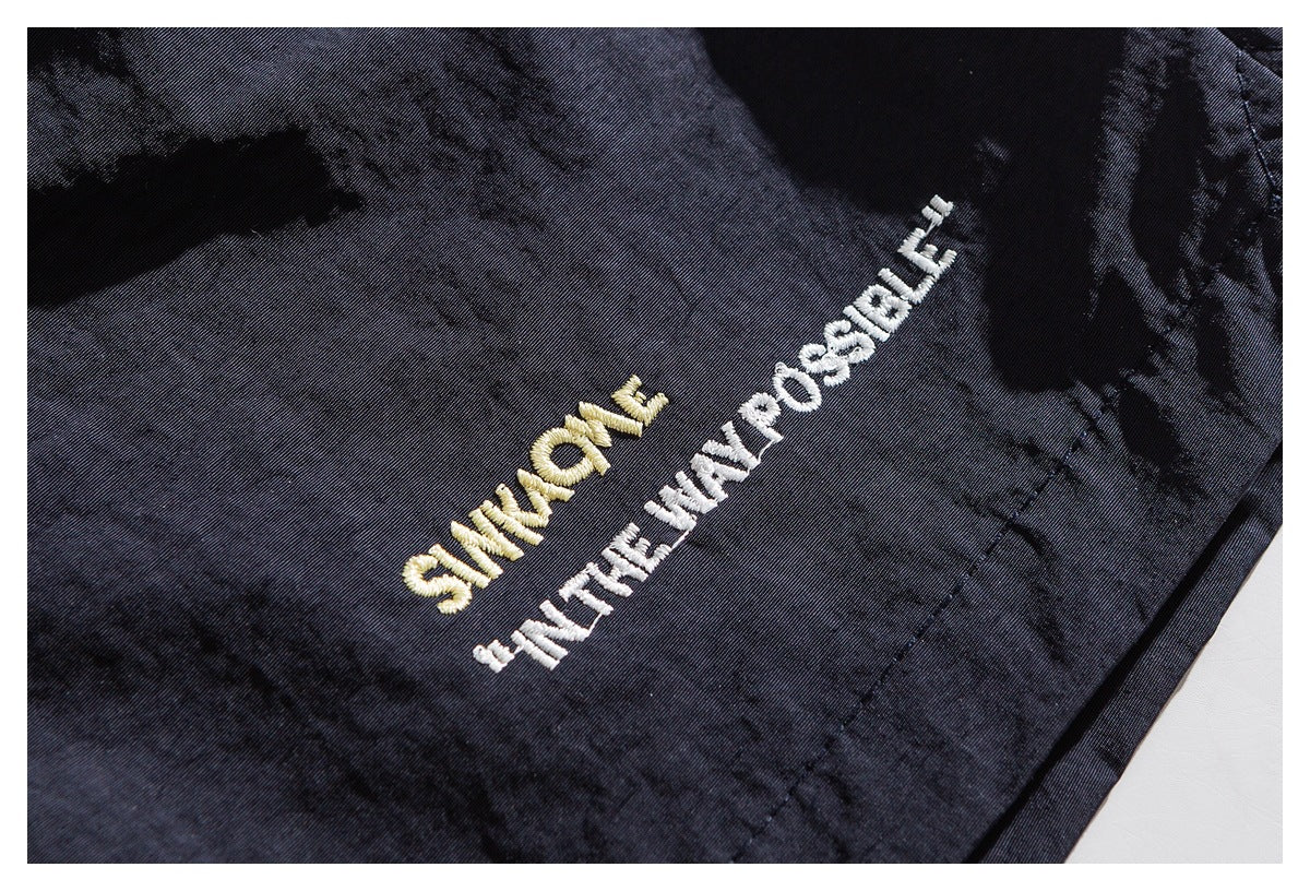 Close-up of dark shorts with gold and white embroidered English lettering on the leg.