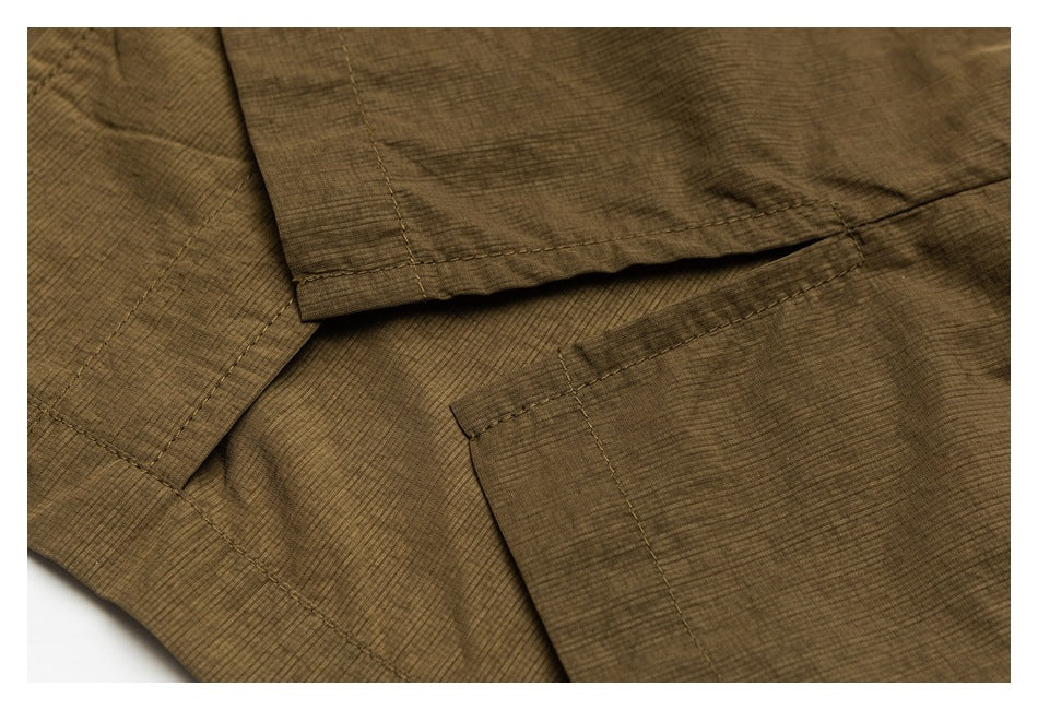 Close-up of olive-brown garment construction showing overlapping panels, stitched edges, and a pocket opening.