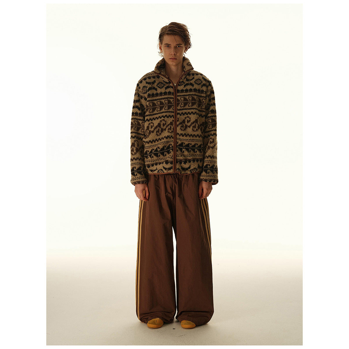 Model wearing a brown and black patterned zip-front jacket with wide brown striped pants.