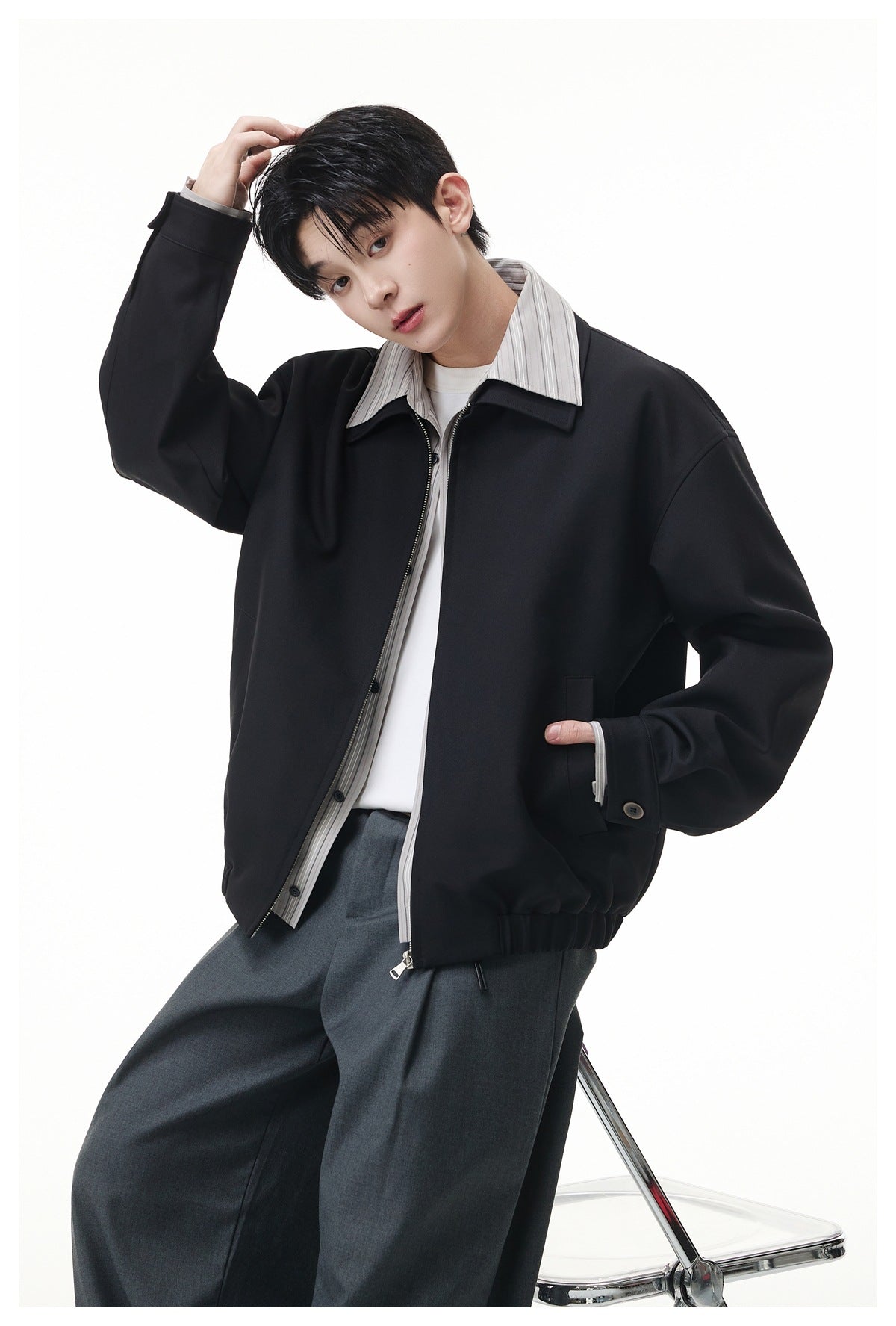 Model wearing a black zip-front jacket with a striped contrast collar and cuffs, styled with a white shirt and charcoal