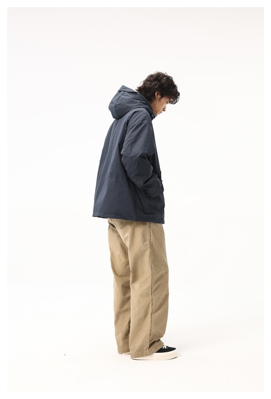 Side and back view of a model wearing a dark navy hooded jacket with tan trousers.