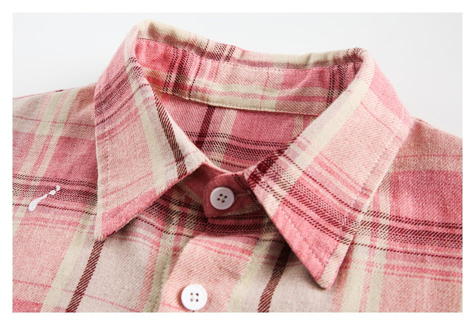 Close-up of a pink plaid shirt collar and white buttons, with small white paint-splatter accents.