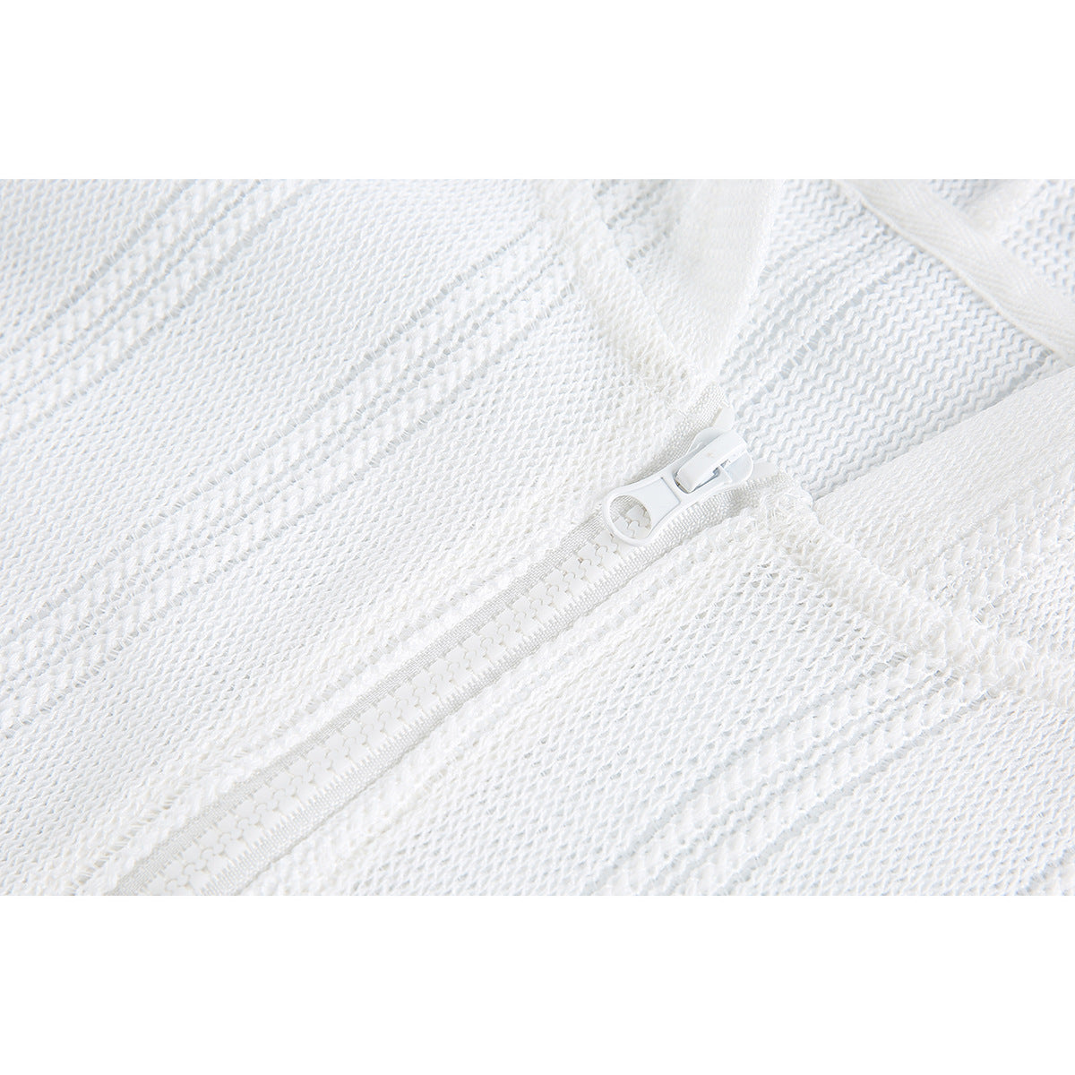 Close-up of a white zipper set into textured white knit fabric.