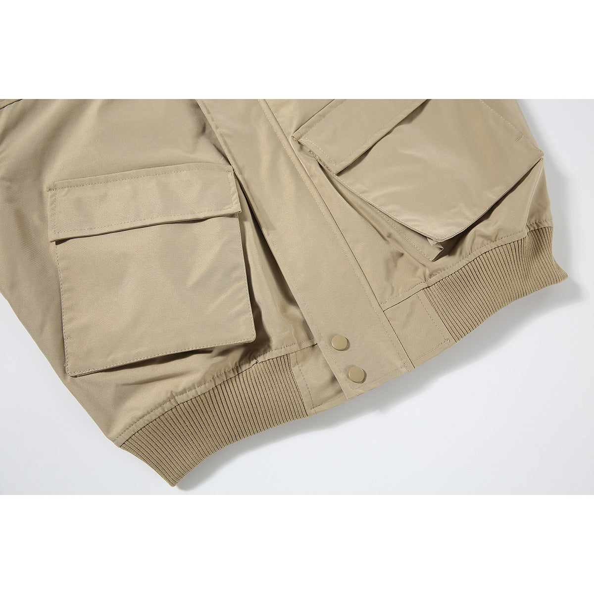 Close-up of a tan bomber jacket showing two flap pockets, snap-front placket, and ribbed hem.