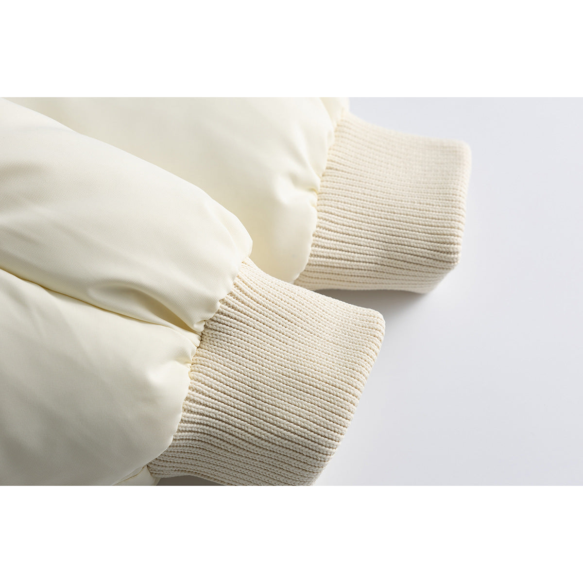 Close-up of the ivory jacket's ribbed knit cuffs beside its padded sleeves.