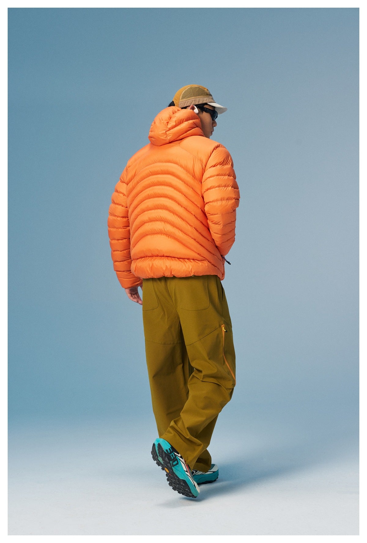 Rear view of a model wearing an orange hooded puffer jacket with curved quilted panels.