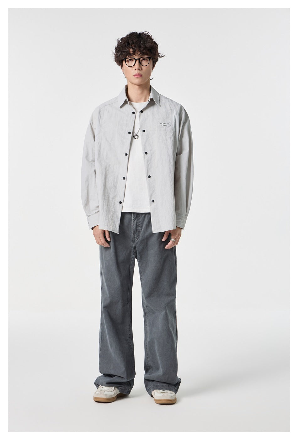 Model wearing a light gray button-front overshirt over a white tee with dark wide-leg jeans.