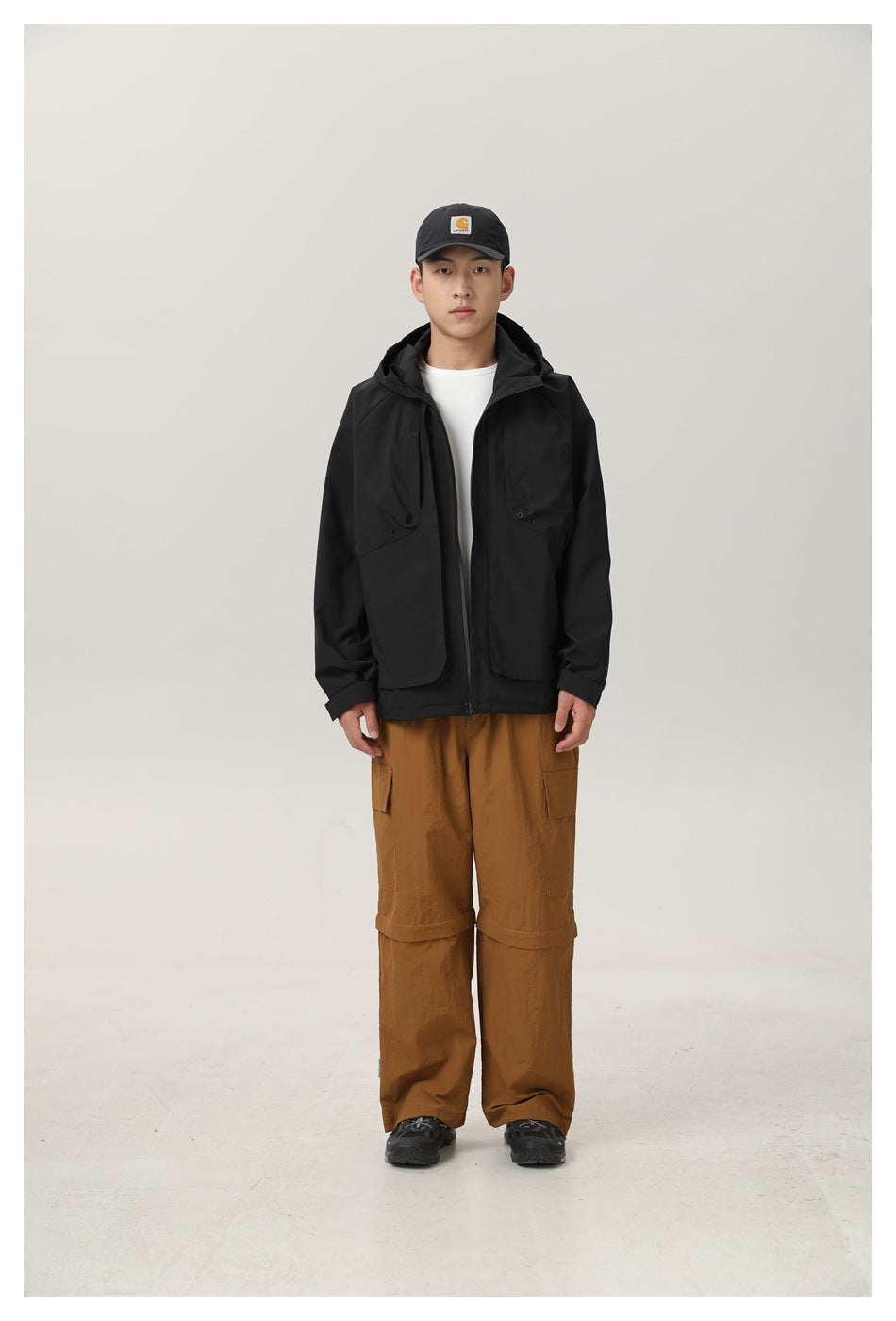 Model wearing a black hooded zip jacket over a white tee with brown cargo pants, front view