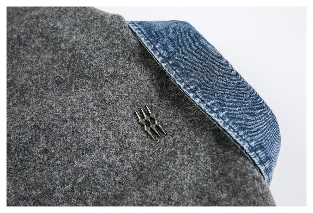 Close-up of a dark gray coat with a blue denim-like panel and a small metal emblem.