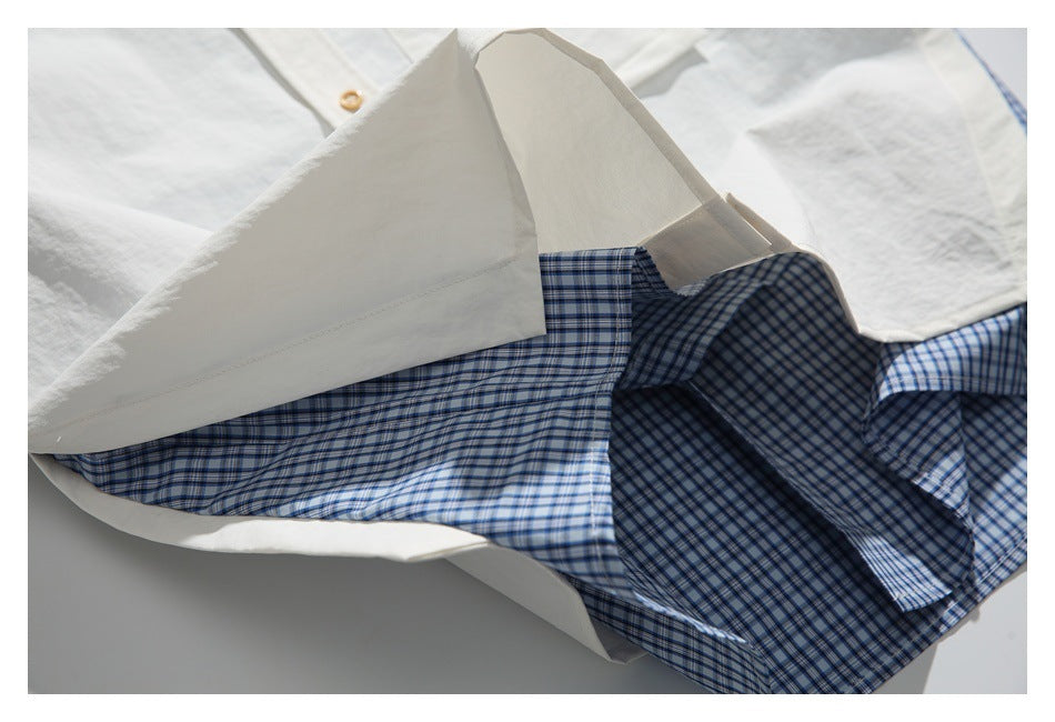 Open white shirt showing a blue-and-white checked inner panel and a tan button.
