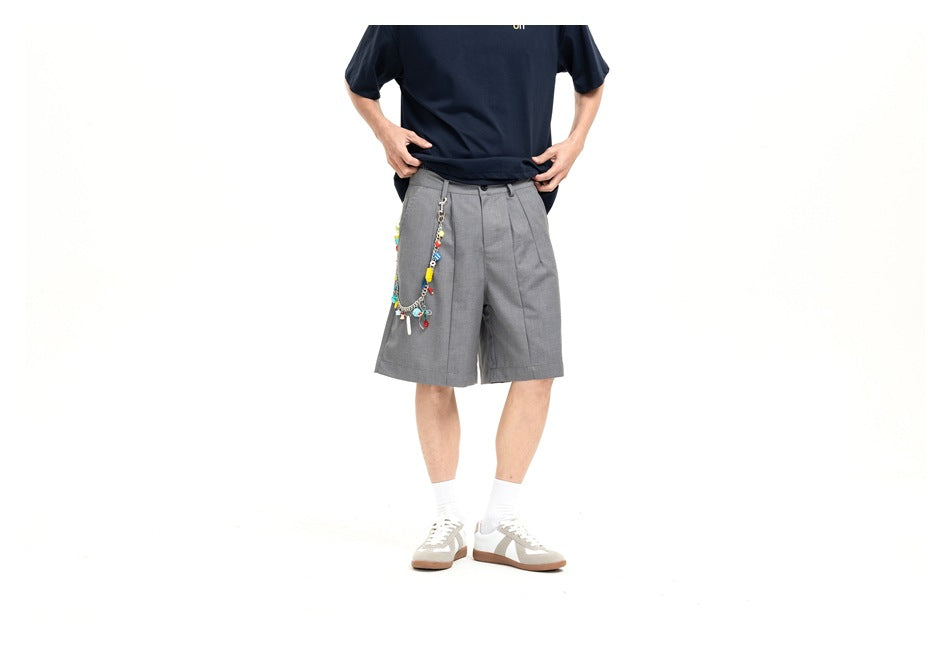 Cropped front view of a model wearing gray pleated shorts with a colorful charm chain and a navy T-shirt.