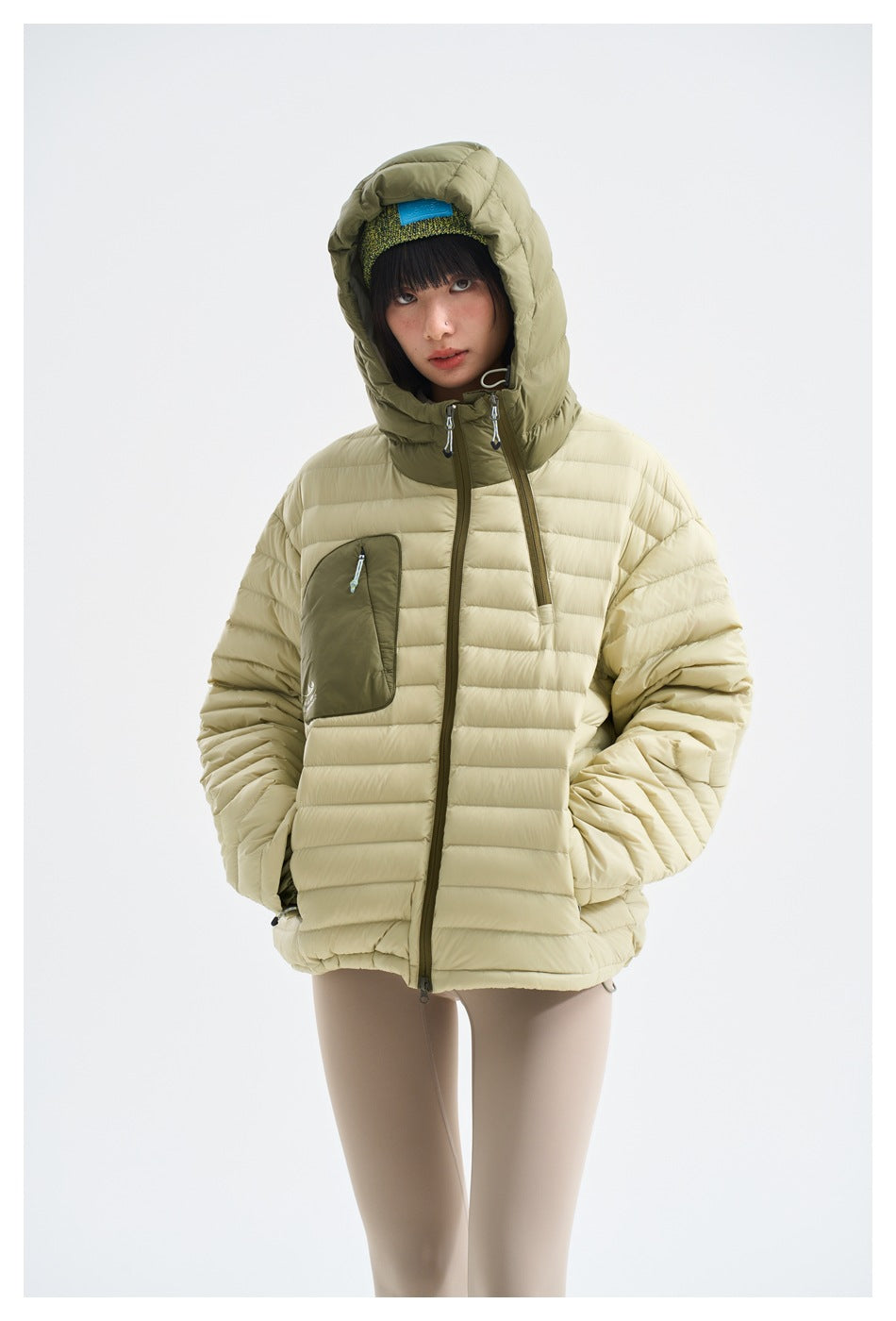 Front view of a model wearing a cream quilted hooded jacket with olive trim and a contrasting chest pocket.