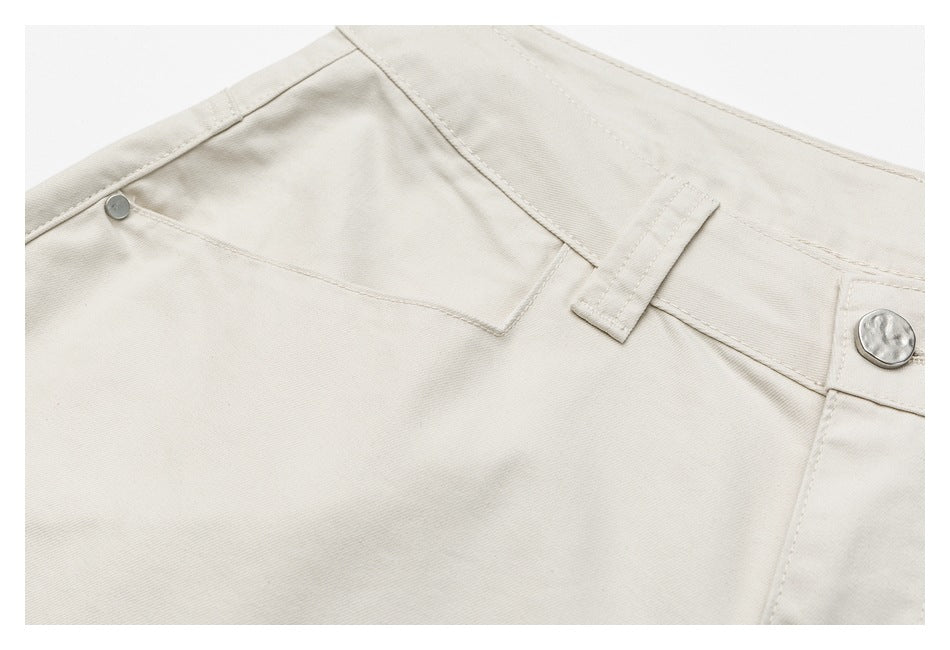 Close-up of ivory trousers showing a front pocket, waistband, belt loop and metal button.