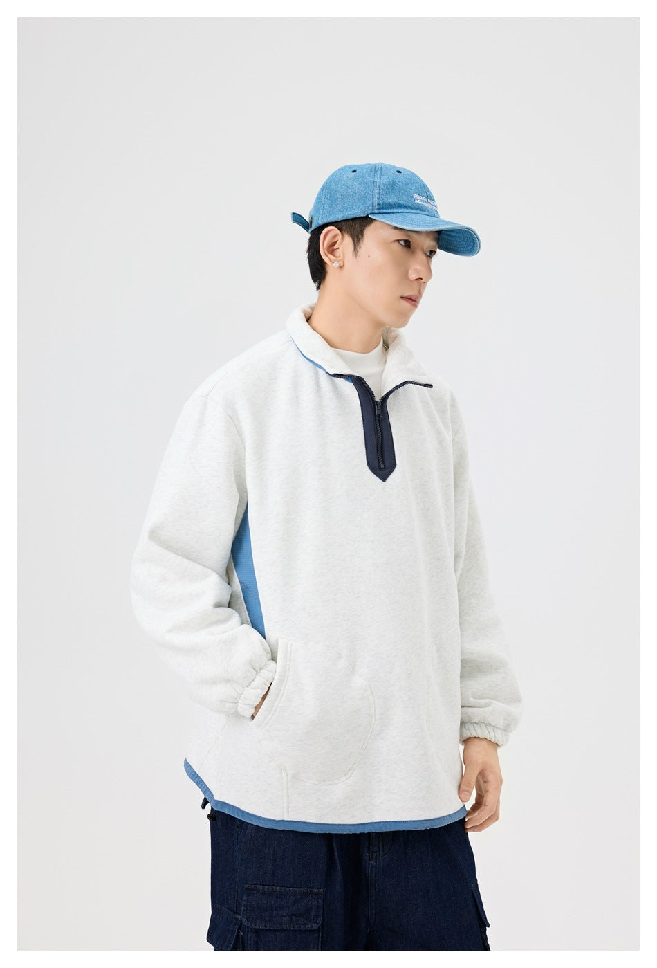 Model wearing a heather gray half-zip sweatshirt with blue trim, side view with a hand in the front pocket