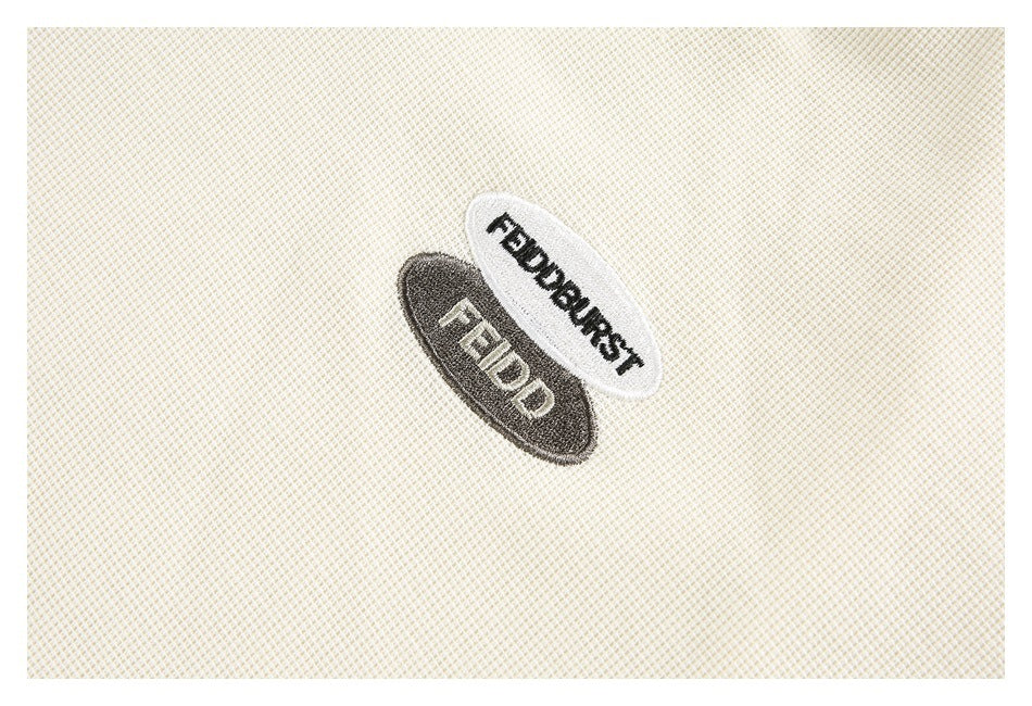Close-up of two embroidered oval patches on cream textured fabric; they read “FIELDBURST” and “FIELD.”