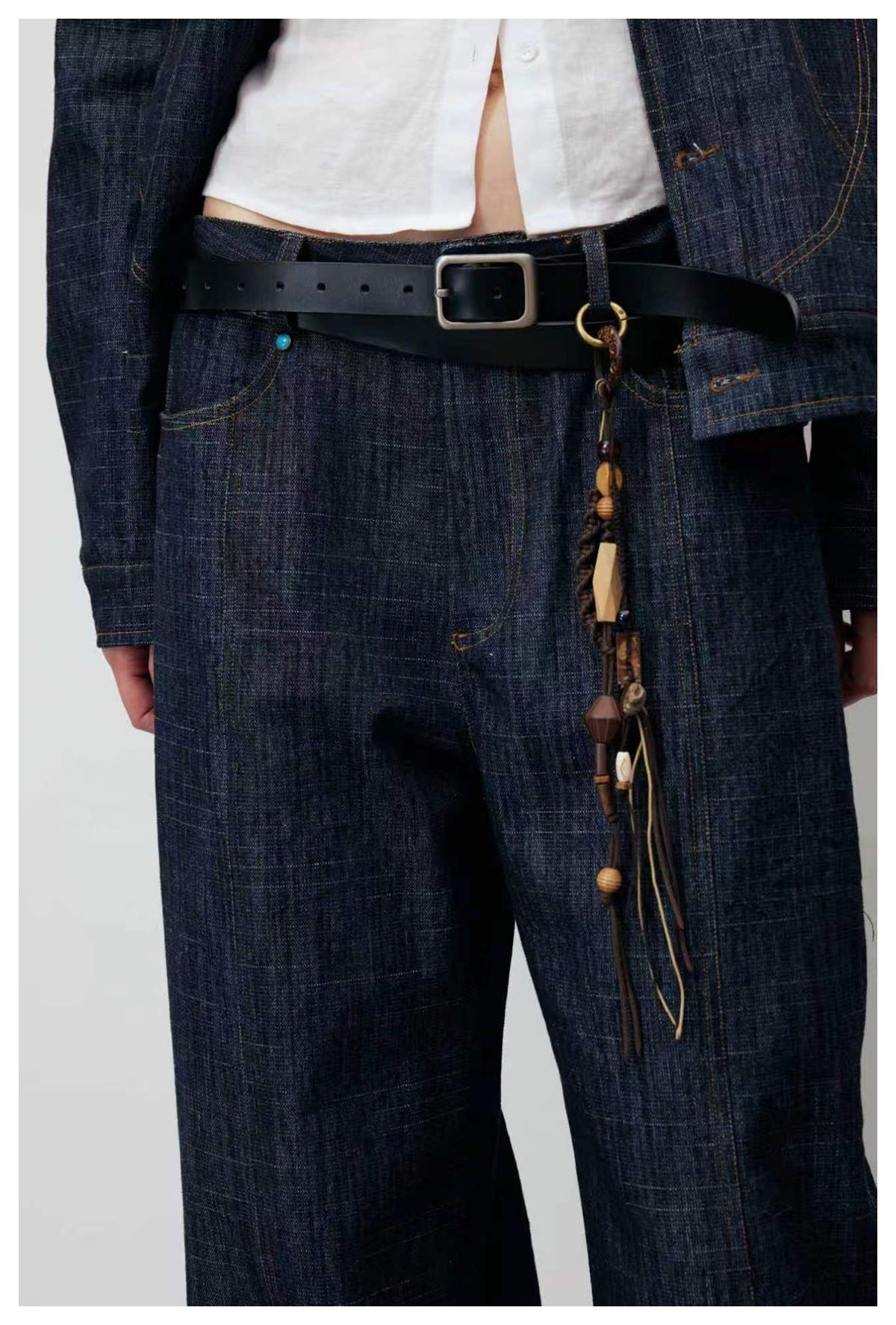 Close front view of dark indigo wide-leg jeans with a black buckle belt and dangling beaded charms.