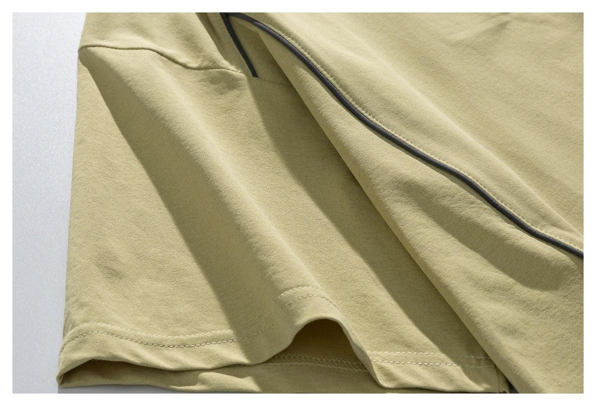Close-up of a pale olive T-shirt sleeve and body with dark piping and stitched hem.