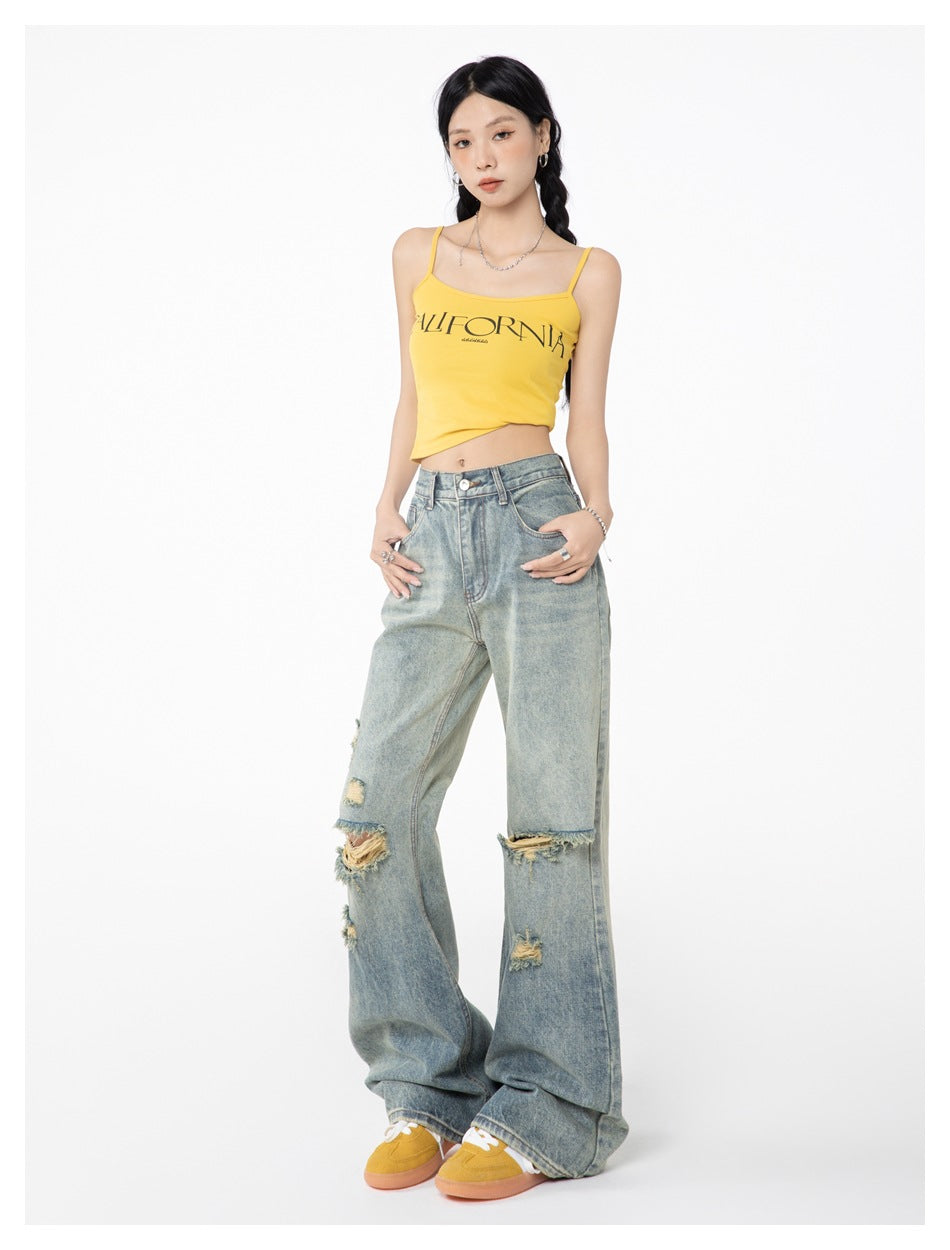 Model wearing light blue distressed flared jeans with a yellow camisole and mustard sneakers, full-length view