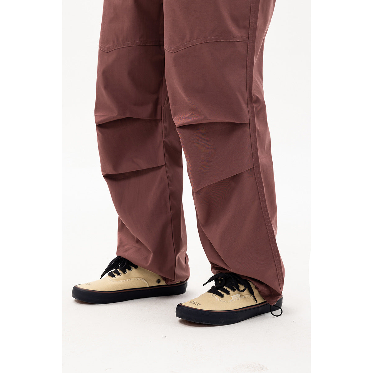 Close-up of mauve cargo pants showing layered leg panels, stitching, loose hems, and beige sneakers.