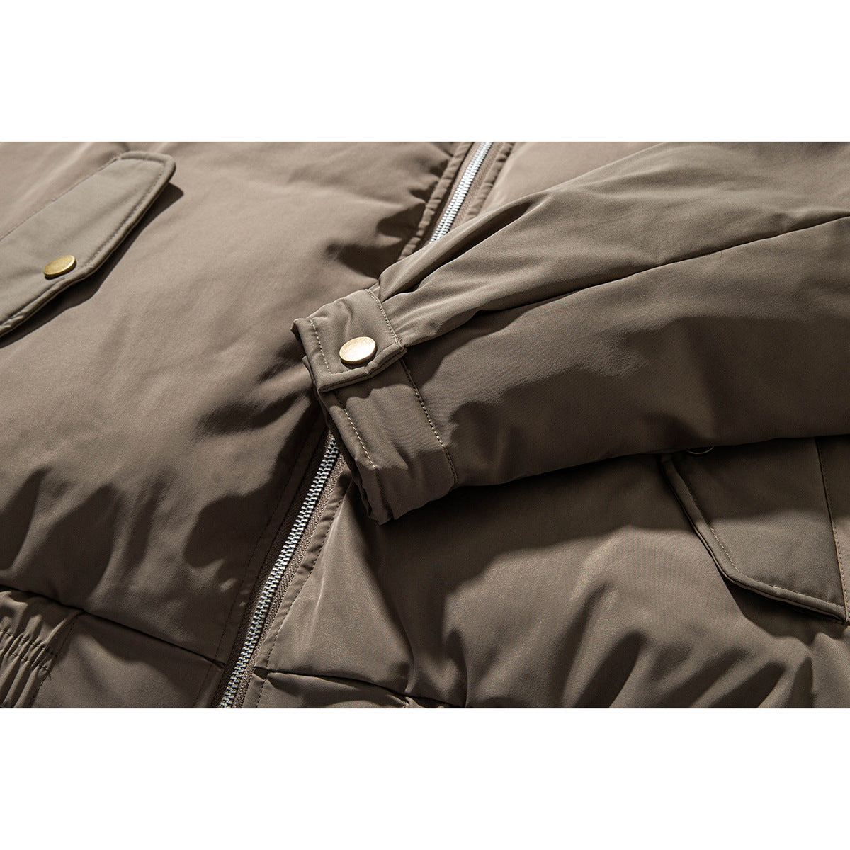 Close-up of a taupe jacket sleeve cuff with a brass-tone snap, zipper, and flap pockets.