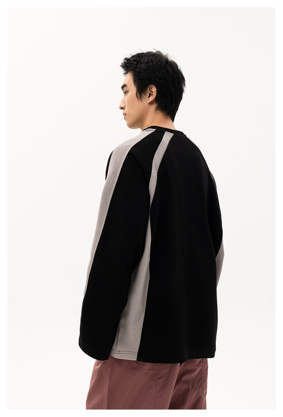 Model shown from behind wearing a black sweatshirt with gray side and sleeve panels and dusty mauve pants.