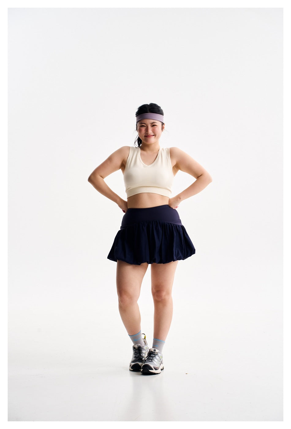 Front view of a woman wearing an ivory sleeveless crop top and navy bubble-hem athletic skirt.