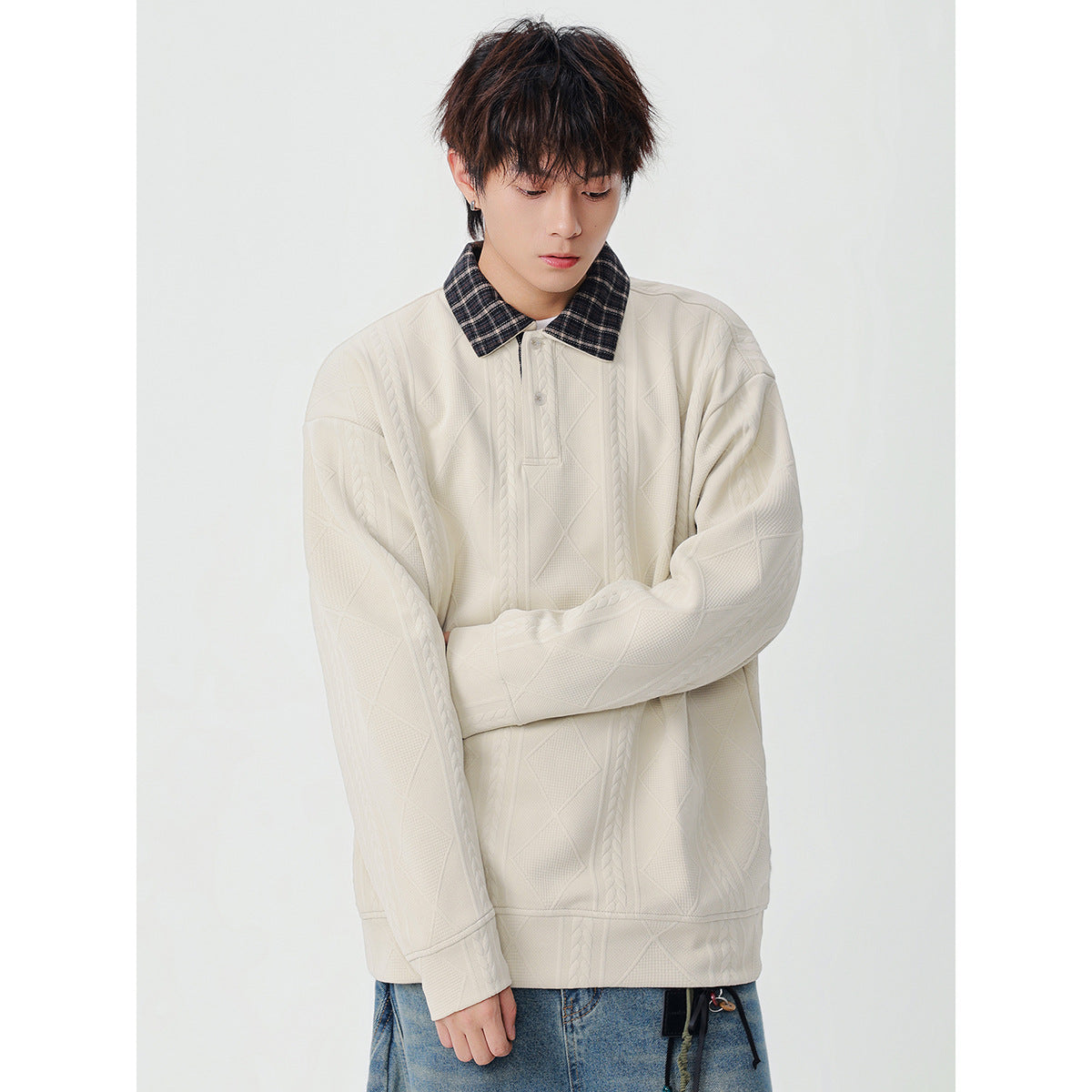 Model wearing an oversized ivory pullover with a dark plaid collar, button placket, and raised cable and diamond patterns.