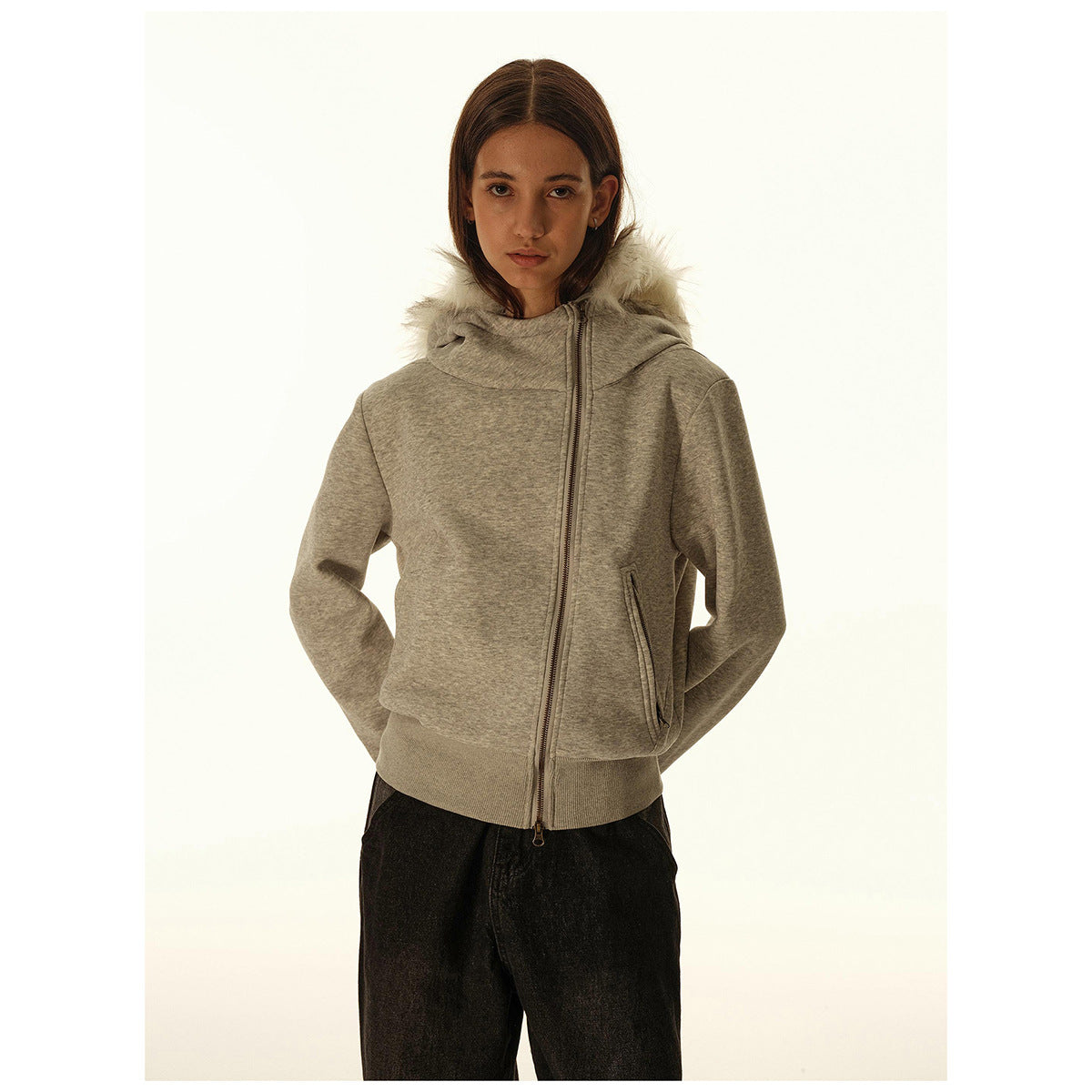 Woman wearing a gray zip-front hoodie with a light fur-trimmed hood and front pockets.
