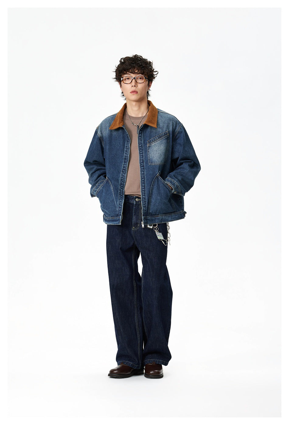 Man wearing a dark blue denim jacket with brown collar over a taupe tee, dark jeans and brown shoes, full-length view