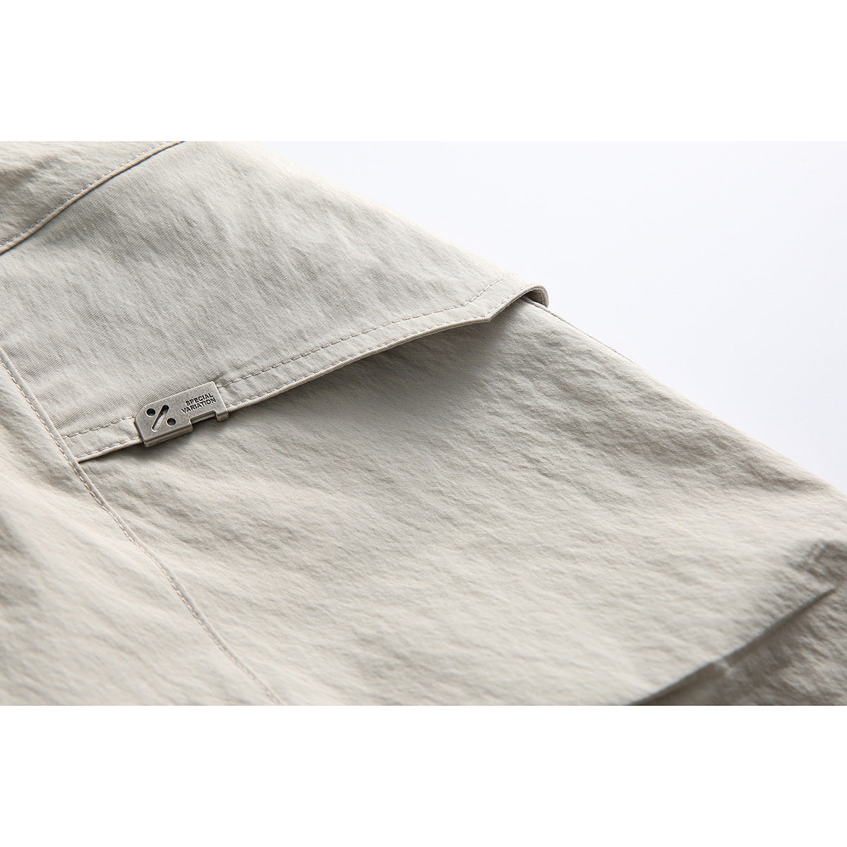 Close-up of a light beige shorts pocket with a small metal tab reading “SPECIAL VARIATION.”