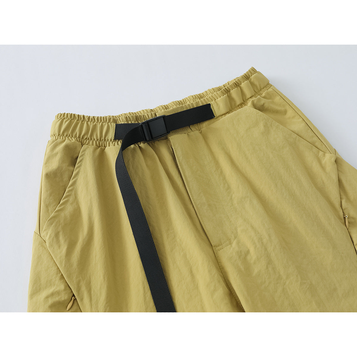 Close-up of mustard-yellow pants showing the elastic waist, black webbing belt, buckle, and front pocket.