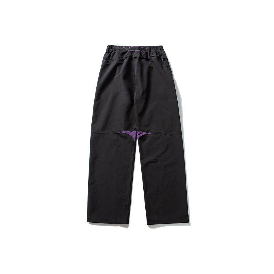 Front view of loose black pants with an elastic waist and purple gusset accent.