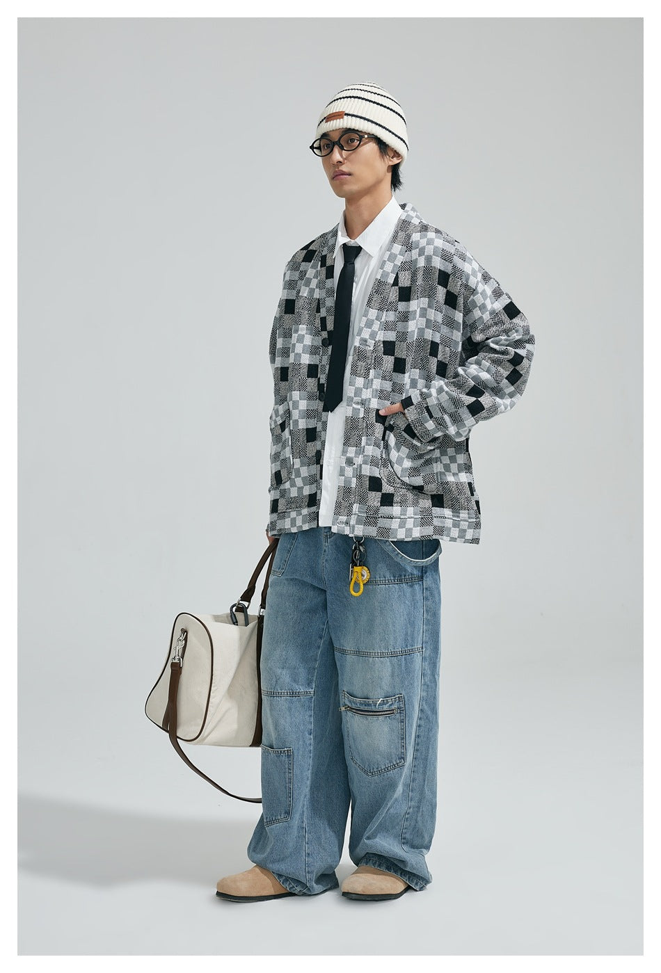 Model wearing a black, gray and white patchwork-check cardigan with blue jeans, shown from the front at an angle.