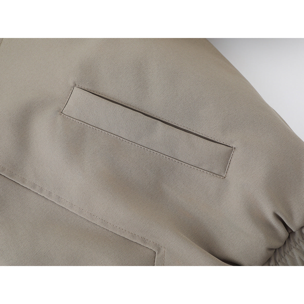 Close-up of a taupe jacket showing a narrow welt pocket and a larger angled pocket.