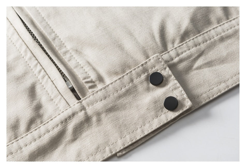 Close-up of a light beige garment with black snap buttons, stitched seams and a zipper edge.