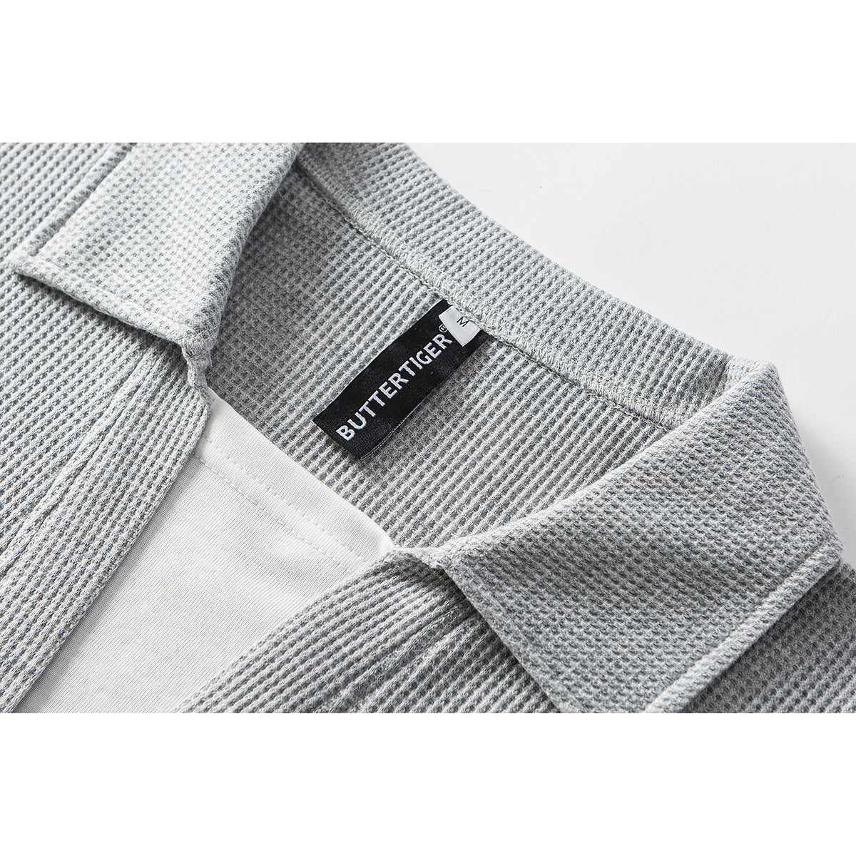 Close-up of a gray textured polo collar, white inner layer, and sewn black neck label.