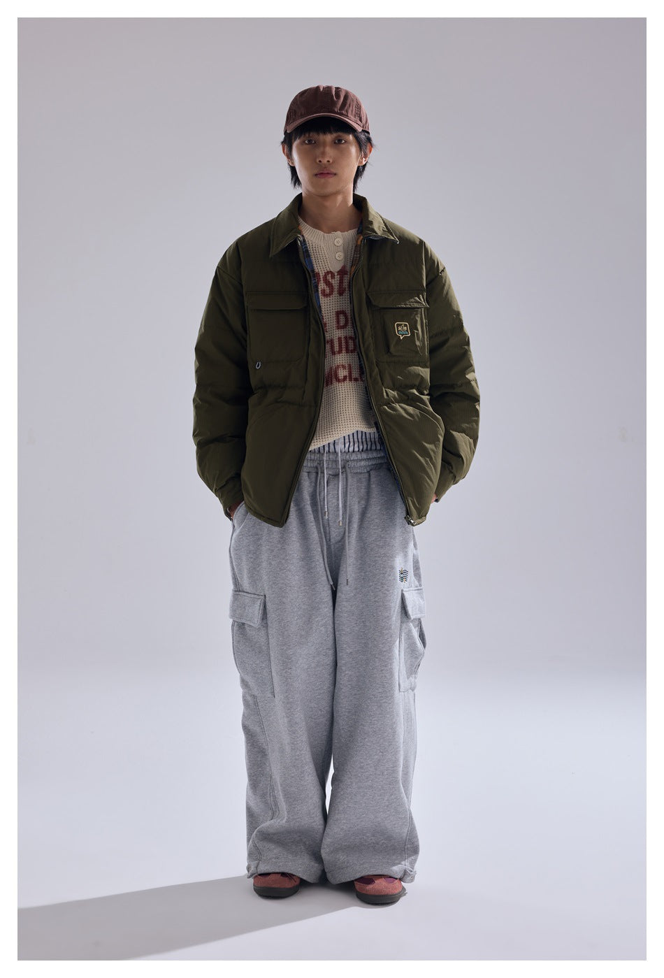 Model wearing the army green zip jacket with a cap, knit top and gray cargo sweatpants, front view