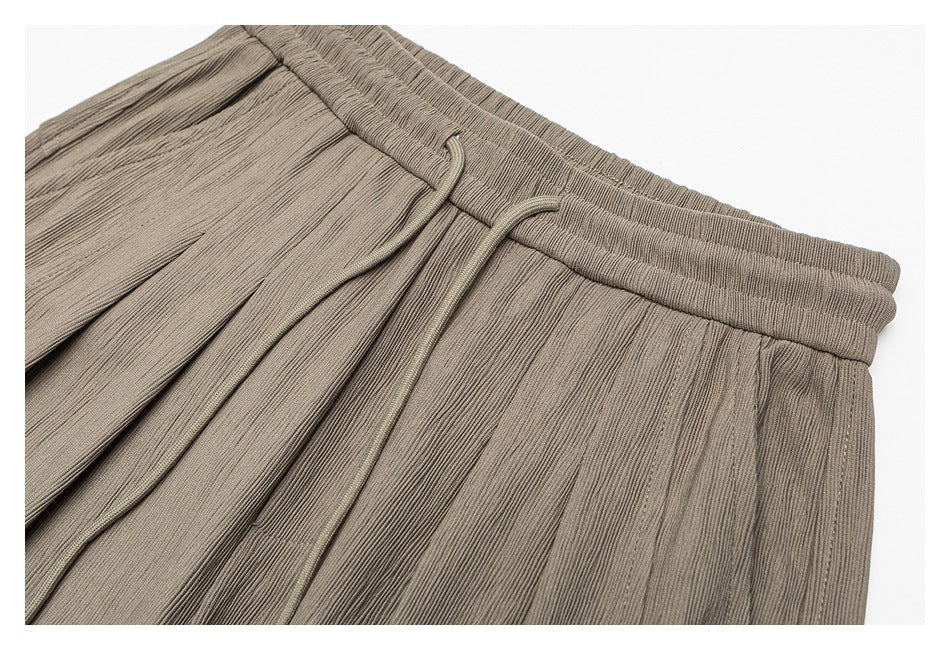 Close-up of taupe pants showing the elastic waistband, drawstring, and front pleats.